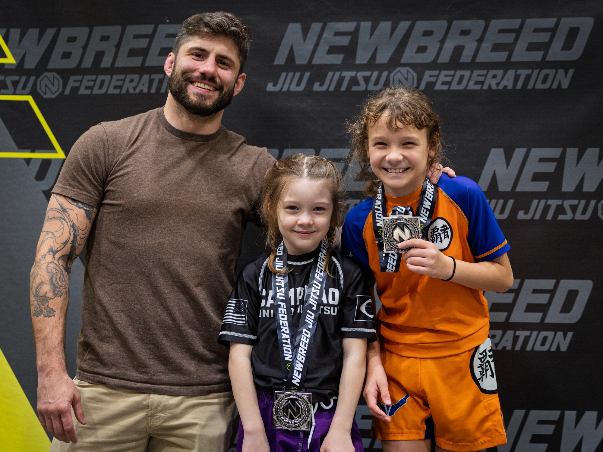 Coach Kevin with two young students holding medals at a New Breed Jiu Jitsu Federation tournament